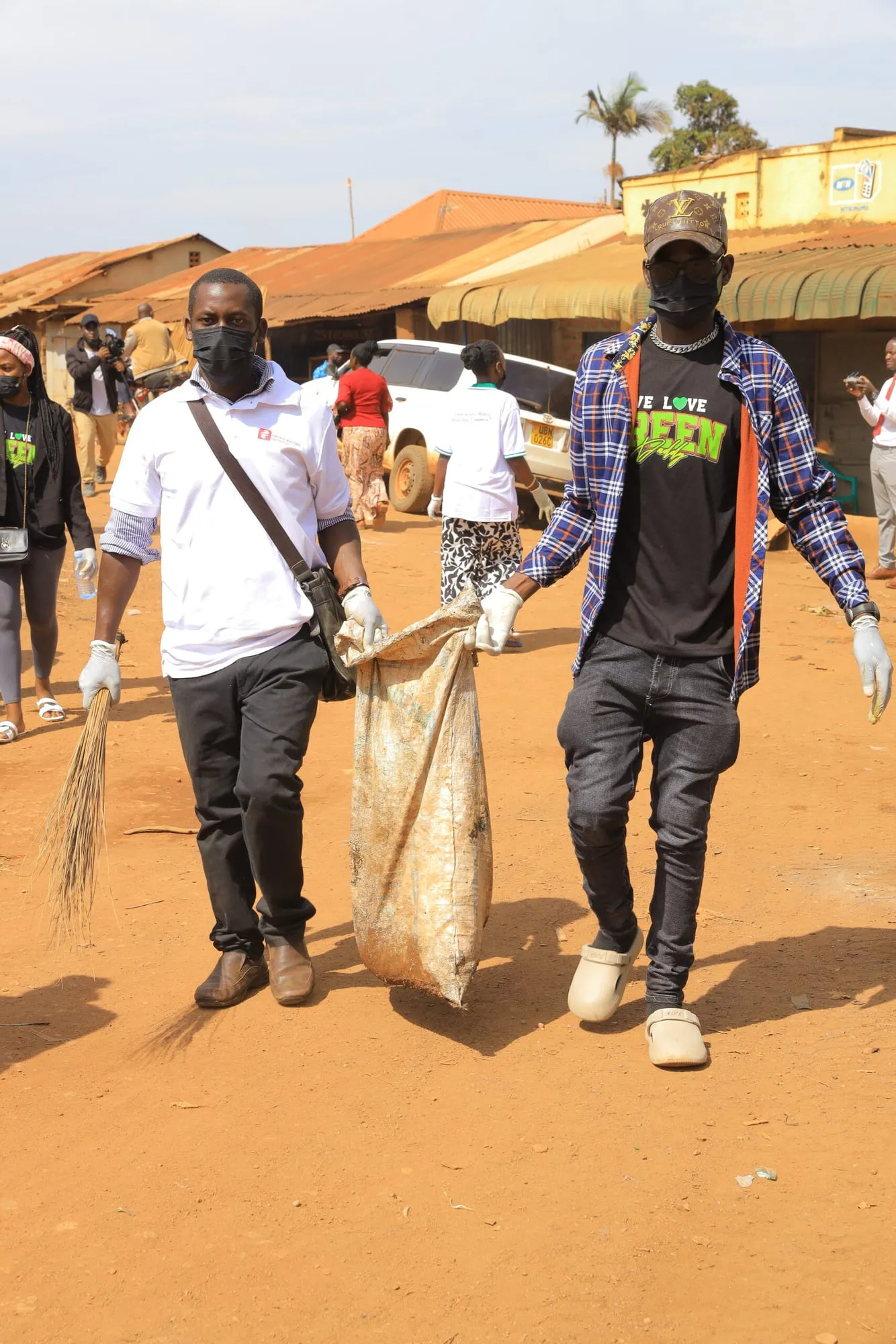Two volunteers carrying sacks during a community clean-up on a dirt road in Bwaise