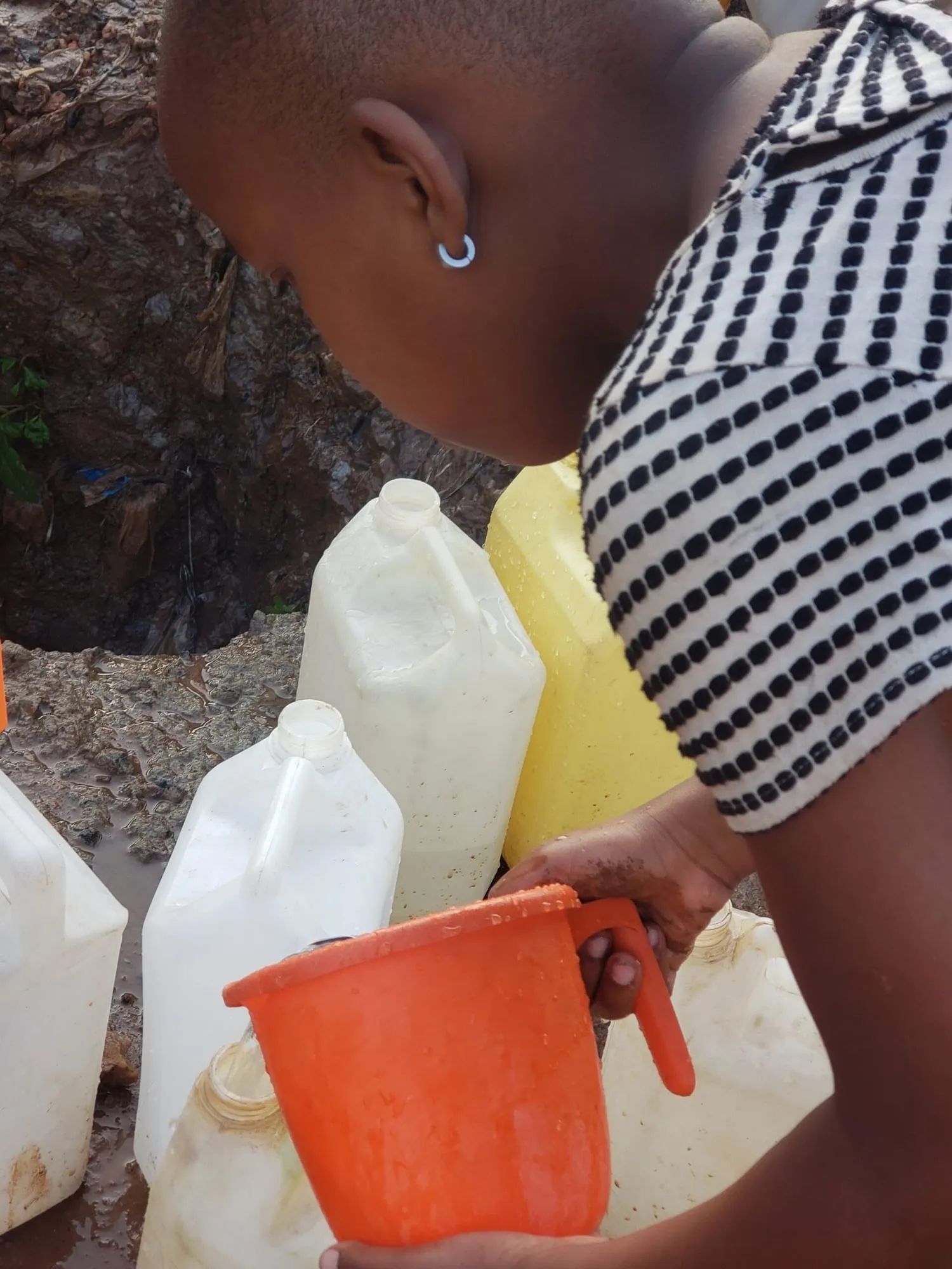 A girl fetching water into yellow jerrycans